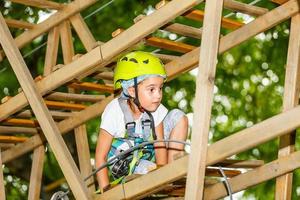 glückliches Schulmädchen, das Aktivität in einem Kletterabenteuerpark an einem Sommertag genießt foto