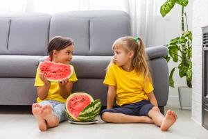 zwei Mädchen essen Wassermelone isoliert auf dem heimischen Hintergrund foto