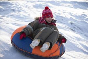 Ein glücklicher Junge in der Luft auf einem Schlauchschlitten im Schnee. Ein Junge rutscht im Winter einen Hügel hinunter. foto