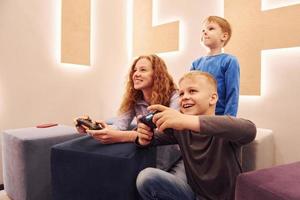 Fröhliche Kinder, die drinnen sitzen und zusammen Videospiele spielen foto