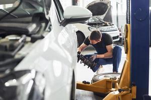 Mann in Arbeitsuniform repariert Auto drinnen. Konzept des Autoservices foto