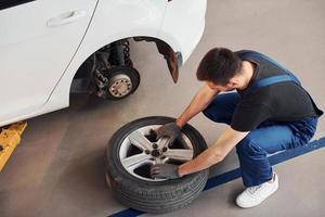 Mann in Arbeitsuniform repariert Auto drinnen. Konzept des Autoservices foto