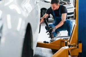 Mann in Arbeitsuniform repariert Auto drinnen. Konzept des Autoservices foto