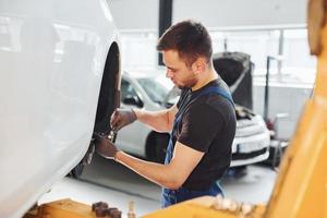 Mann in Arbeitsuniform repariert Auto drinnen. Konzept des Autoservices foto