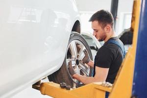 Mann in Arbeitsuniform, der drinnen das Autorad wechselt. Konzept des Autoservices foto