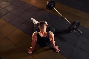 Draufsicht eines starken Mannes in sportlicher Kleidung, der auf dem Boden sitzt und eine Pause im Fitnessstudio macht foto