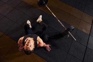 Draufsicht eines starken Mannes in sportlicher Kleidung, der auf dem Boden sitzt und eine Pause im Fitnessstudio macht foto