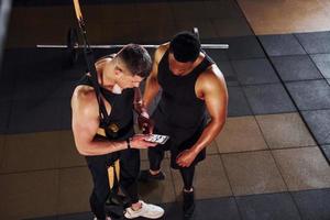 eine Pause machen und telefonieren. afroamerikanischer mann mit weißem kerl hat trainingstag im fitnessstudio foto