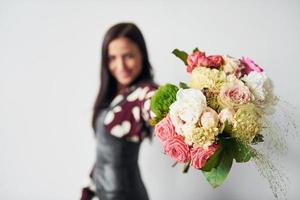 schöne junge Brünette im schwarzen Rock, die drinnen vor weißem Hintergrund steht, mit Blumenstrauß in den Händen foto