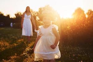 schöner Lichtstrahl. mutter mit jungen und mädchen, die an sonnigen sommertagen freizeit auf dem feld verbringen foto