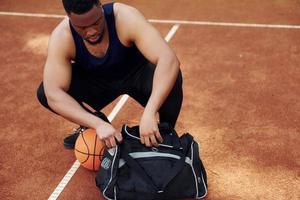 sitzt mit schwarzer Tasche und bereitet sich auf das Spiel vor. afroamerikaner spielt basketball auf dem platz im freien foto