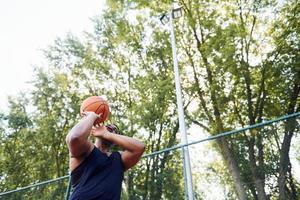 wolkiges Wetter. afroamerikaner spielt basketball auf dem platz im freien foto