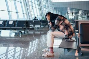 Trauriges junges Mädchen, das weint, wenn es auf dem modernen Flughafen sitzt foto