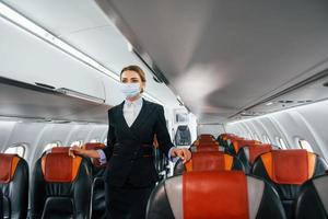 in Maske. junge Stewardess über die Arbeit im Passagierflugzeug foto