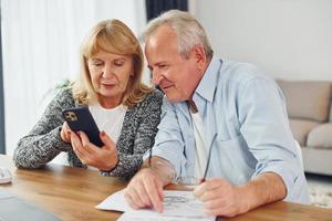 Blick aufs Telefon und Zeichnen. Senior Mann und Frau sind zusammen zu Hause foto