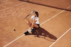 auf dem Boden sitzen. Tennisspielerin ist tagsüber auf dem Platz foto