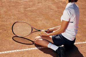 auf dem Boden sitzen. Tennisspielerin ist tagsüber auf dem Platz foto