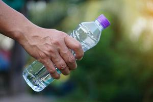 nahaufnahmehand hält trinkwasserflasche mit lila kappe. Konzept, Trinkwasser für Gesundheit, gesunder Lebensstil. Durst löschen, Müdigkeit reduzieren, Körper erfrischen. foto