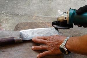Nahhände schärfen ein Messer mit einer elektrischen Schärfer-Schleifmaschine in Bewegung, Aktion des Funkens. Konzept, traditioneller Stil des Befestigungswerkzeugs. foto