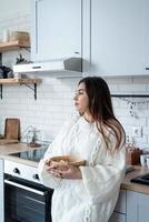 Frau in warmweißem Winterpullover, die zu Hause in der Küche steht foto