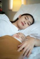 Eine Mutter muss mit ihrem neugeborenen Baby schlafen und sich ausruhen. im weißen schlafzimmer, warmes sonnenlicht am abend des tages. foto