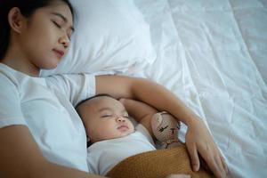 Eine Mutter muss mit ihrem neugeborenen Baby schlafen und sich ausruhen. im weißen schlafzimmer, warmes sonnenlicht am abend des tages. foto