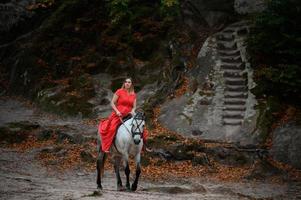 Dovbush-Felsen und Reiten, eine Frau, die in einem roten Kleid mit bloßen Füßen auf einem Pferd reitet. foto