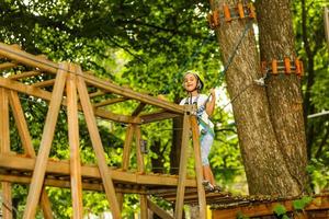 glückliches Schulmädchen, das Aktivität in einem Kletterabenteuerpark an einem Sommertag genießt foto