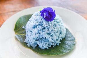 asiatische taubenflügel mit thailändischem reis, gekocht auf grünem blatt auf teller blauer reis und schmetterlingserbsenblume für gesunde naturkost foto
