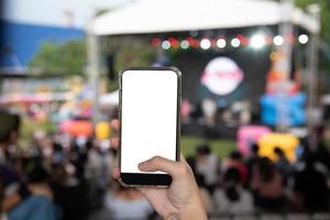 hand, die mobiles smartphone mock up weißen bildschirm leer auf musikfestival im gartenhintergrund hält. foto