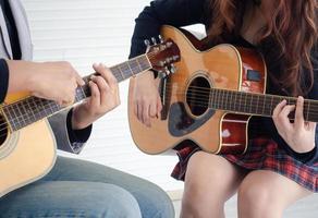 Frau übt, während sie auf einem Stuhl sitzt. die handberührenden saiten des lehrers erklären schnüre, die grundlagen des gitarrenspiels, das lebensstilkonzept foto