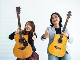 porträt asiatischer duo-künstler mit einer akustischen gitarre, die auf einem weißen hintergrund sitzt und die geste des klopfens nach oben für musik, künstler, musikerkonzept zeigt foto