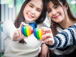 selektiver fokus, junges asiatisches lesbisches paar, das ein regenbogenherz hält, symbolisiert die lgbt-gemeinschaft, im wohnzimmer zu hause, den lebensstil von paaren, die frauen lieben, die in romantischer liebe und spaß glücklich sind foto