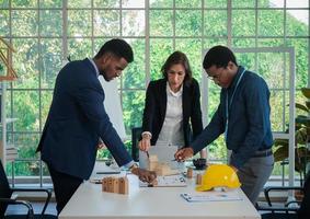 Die gemischtrassigen Kollegen von Geschäftsleuten machen im Büro ein Brainstorming mit Hausmodellen und Bauplänen. Professionelles Bauteam bespricht die Anordnung der Hausanschlüsse am Neubau. foto