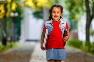 porträt eines attraktiven kaukasischen kleinen studentenmädchens mit schönen braunen augen. glückliches lächelndes kind, das kamera betrachtet - nahaufnahme, draußen. foto