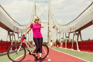 Rückansicht einer jungen schlanken Frau, die am Fahrrad auf Brückenhintergrund steht. aktives lebensstil- und urlaubskonzept. foto