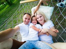 Familie, die sich an einem sonnigen Sommertag im Garten des Ferienhauses auf einer Hängematte niederlegt und entspannt. familie entspannen im freien, gesunder und wellness-lebensstil. foto