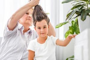 entzückendes verspieltes kleines Mädchen mit glücklicher Oma mittleren Alters zu Hause. süße kleine Enkelin im Vorschulalter mit aufgeregter älterer Großmutter. foto