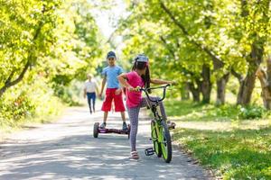 Mädchen auf einem Fahrrad und ein Junge auf einem Gyroskop fahren zusammen foto