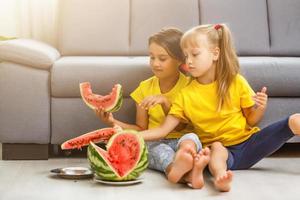 zwei Mädchen essen Wassermelone isoliert auf dem heimischen Hintergrund foto