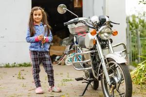 kleines Mädchen, das ein Motorrad repariert, Studentin in der Motorradmechanik foto