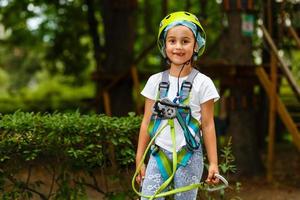 entzückendes kleines mädchen, das ihre zeit im kletterabenteuerpark an warmen und sonnigen sommertagen genießt foto