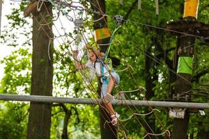 entzückendes kleines mädchen, das ihre zeit im kletterabenteuerpark an warmen und sonnigen sommertagen genießt foto