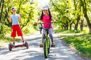 Mädchen auf einem Fahrrad und ein Junge auf einem Gyroskop fahren zusammen foto