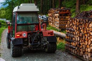 selbstgemachter improvisierter Traktoranhänger aus starkem Metall, mit vorbereitetem Brennholz gestapelt und zum Schutz mit einer Plane bedeckt, die im Hinterhof des Familienhauses, umgeben von ungemähtem Gras, zurückgelassen wurde. foto