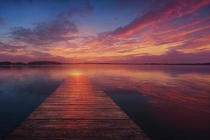 farbenfroher Holzsteg an einem See, der bei Sonnenuntergang völlig ruhig ist foto
