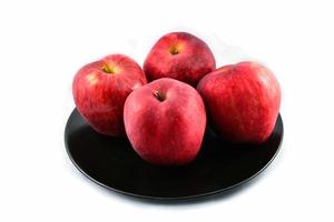frischer roter Apfel auf schwarzem Teller isoliert auf weißem Hintergrund foto