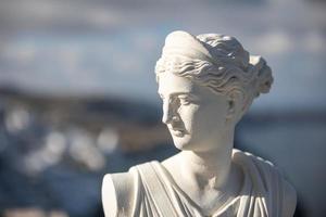 weiße artemis-statue, diana-göttin mit verschwommenem blick auf santorini fira in griechenland. historisches porträt und traditionelle kunst in griechenland foto