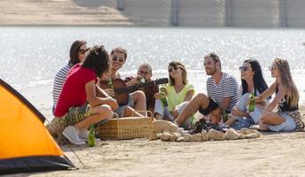 sommer, ferien, urlaub, musik, fröhliches menschenkonzept - gruppe von freunden mit gitarre, die spaß am strand haben foto