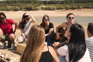 sommer, ferien, urlaub, musik, fröhliches menschenkonzept - gruppe von freunden mit gitarre, die spaß am strand haben foto